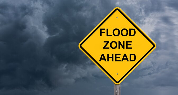 Yellow flood zone ahead caution sign with storm background