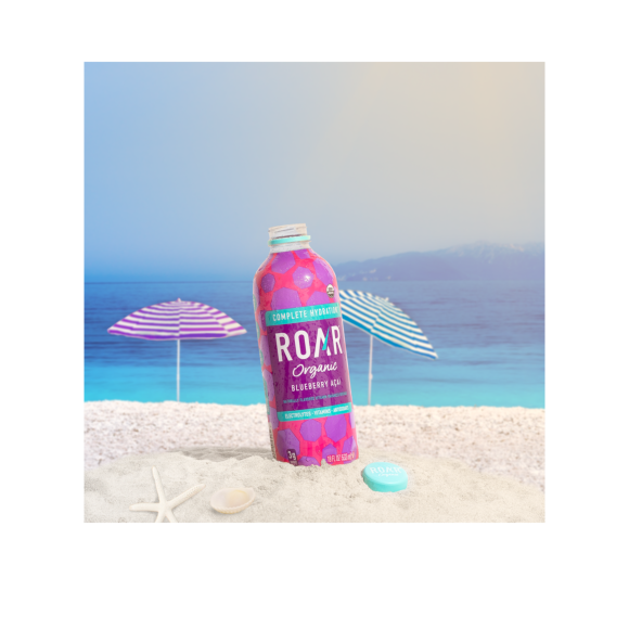 bottle of roar organic blueberry acai drink on a beach Image2